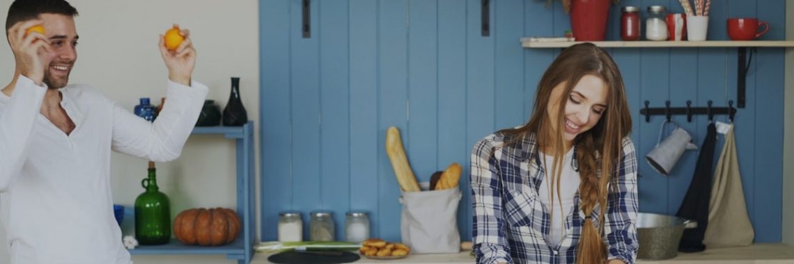 Attractive loving couple having fun in the kitchen. Handsome man juggle with fruits to impress his girlfriend at home