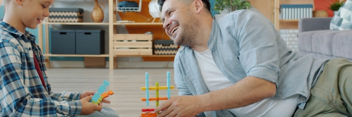 Adult man and little boy playing with wooden toys at home talking laughing enjoying game in free time. Communication and family activities concept.